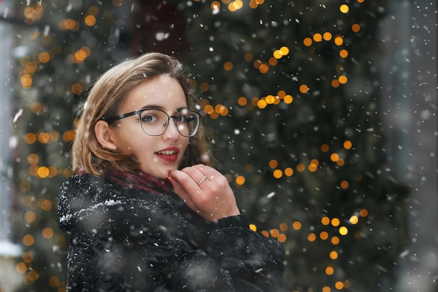 Mooie jonge vrouw draagt een bril die tijdens sneeuwval in de stad loopt. Lege ruimte