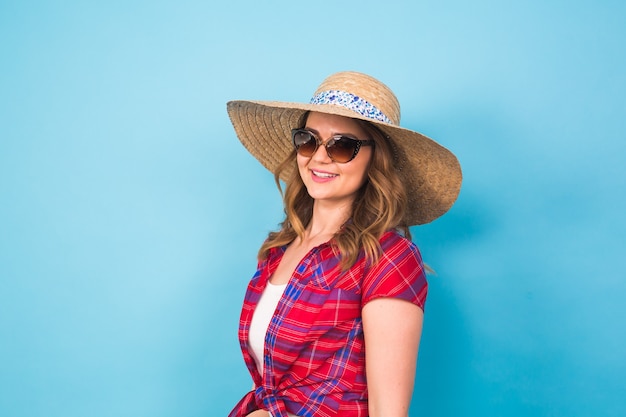 Mooie jonge vrouw draagt in zomerjurk en strohoed lacht op blauwe achtergrond met kopieerruimte.