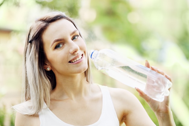 Mooie jonge vrouw drinkt water uit een fles met een wazige vegetatieachtergrond