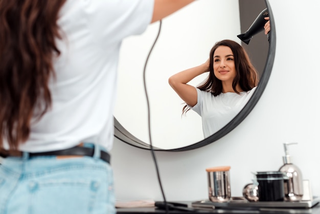 Mooie jonge vrouw droogt haar mooie haar en kijkt in de spiegel