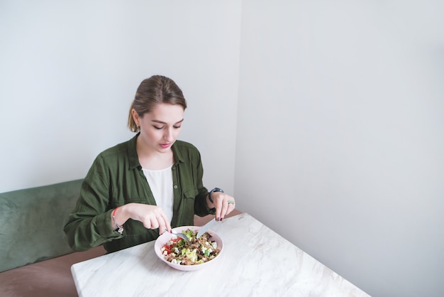 mooie jonge vrouw een smakelijke salade eten in restaurant met licht interieur.