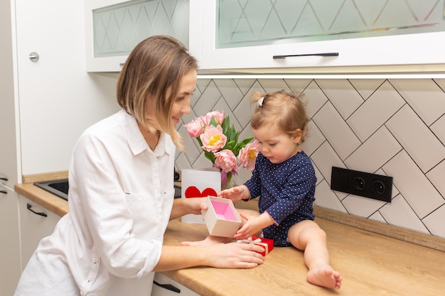 Mooie jonge vrouw en haar charmante dochtertje glimlachen in het interieur van de witte keuken