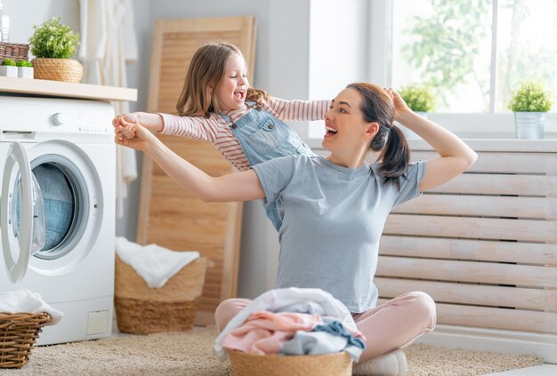 Mooie jonge vrouw en kleine helper van het kindmeisje glimlachen terwijl ze thuis de was doen