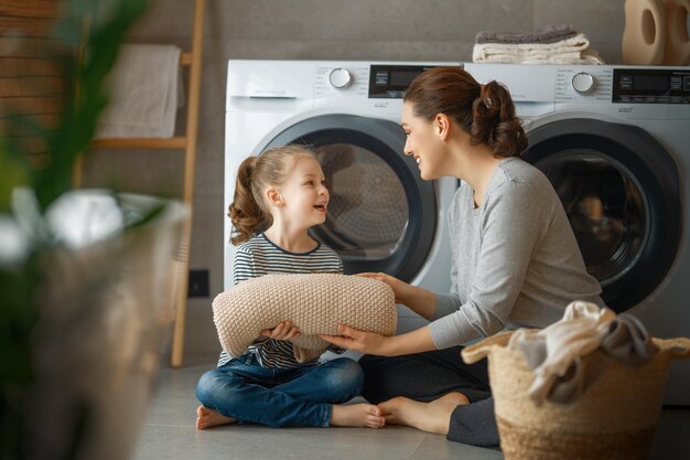 Mooie jonge vrouw en kleine helper van het kindmeisje hebben plezier en glimlachen terwijl ze thuis de was doen