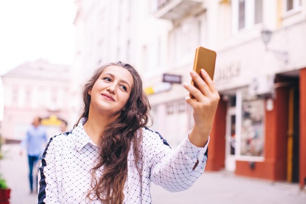 Mooie jonge vrouw gekleed in casual stijl maakt selfie terwijl ze door de stad loopt