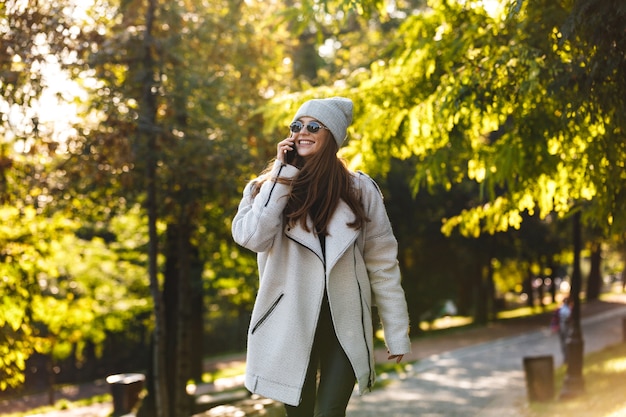 Mooie jonge vrouw gekleed in herfst jas en hoed buiten wandelen, praten op een mobiele telefoon