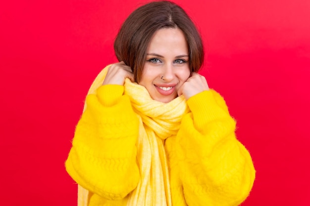 Mooie jonge vrouw, gekleed in warme gele wollen trui op rode achtergrond koude winter portret