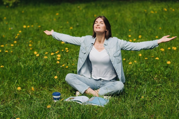 Mooie jonge vrouw geniet van de natuur zittend in het park met boek en koffie