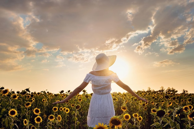Mooie jonge vrouw genieten van de natuur op het veld met zonnebloemen bij zonsondergang