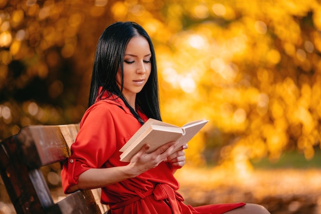 Mooie jonge vrouw genieten van in de herfst kleuren zonnig bos lezen van een boek in haar hand.