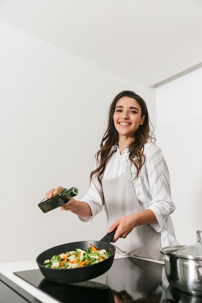 Mooie jonge vrouw gezond diner koken in de keuken, met behulp van koekenpan