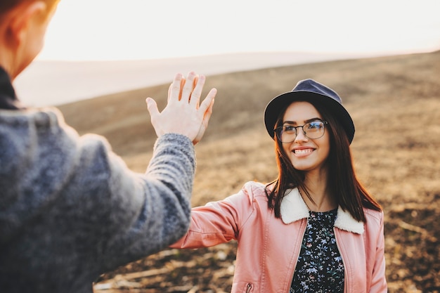 Mooie jonge vrouw glimlachend en high five geven aan anonieme vriend terwijl ze samen in de wei staan. Vrouw high five met vriendje in veld