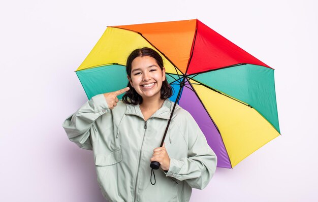 Mooie jonge vrouw glimlachend vol vertrouwen wijzend naar eigen brede glimlach. regen en paraplu concept