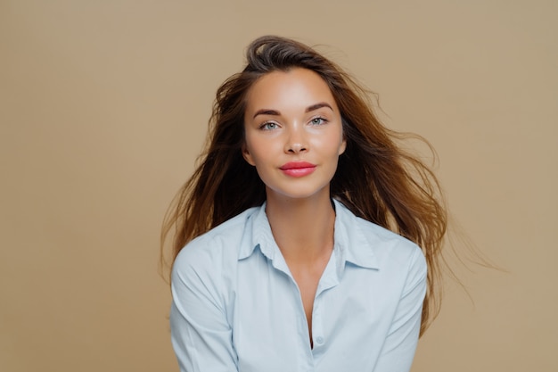 Mooie jonge vrouw heeft lang golvend haar zwevend in de wind, gekleed in elegant blauw shirt
