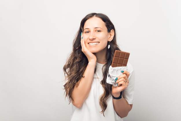 Mooie jonge vrouw houdt een reep chocolade vast en lacht naar de camera.