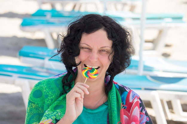 Foto mooie jonge vrouw houdt kleurrijke lolly op het strand en glimlacht