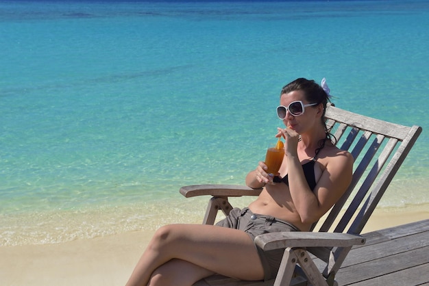 Mooie jonge vrouw in bikini liggend op een ligstoel met een drankje aan zee