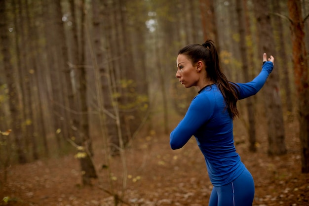 Mooie jonge vrouw in blauw trainingspak die zich uitstrekt voor de training in het herfstbos