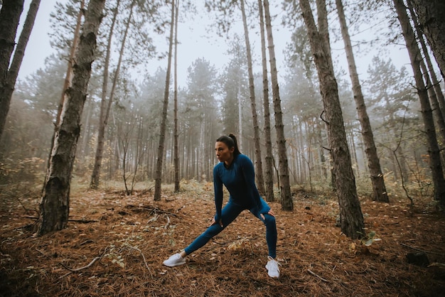 Mooie jonge vrouw in blauw trainingspak die zich uitstrekt voor de training in het herfstbos