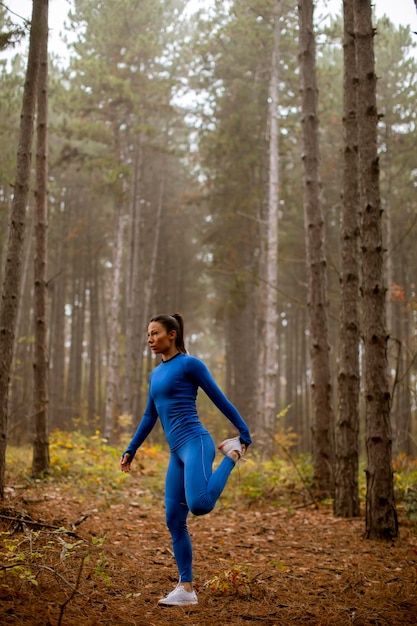 Mooie jonge vrouw in blauw trainingspak die zich uitstrekt voor de training in het herfstbos