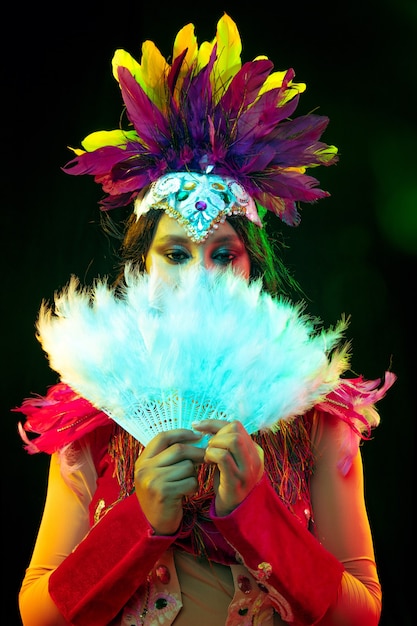 Mooie jonge vrouw in carnavalsmasker en maskeradekostuum in kleurrijke lichten