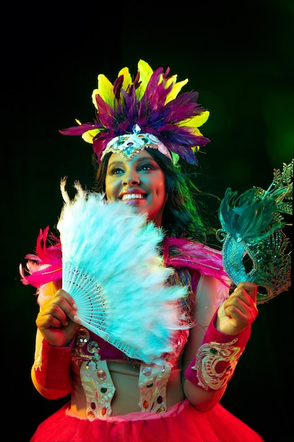 Mooie jonge vrouw in carnavalsmasker en maskeradekostuum in kleurrijke lichten