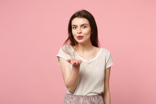 Mooie jonge vrouw in casual lichte kleding poseren geïsoleerd op pastel roze muur achtergrond, studio portret. Mensen oprechte emoties levensstijl concept. Bespotten kopie ruimte. Blazen luchtkus verzenden.