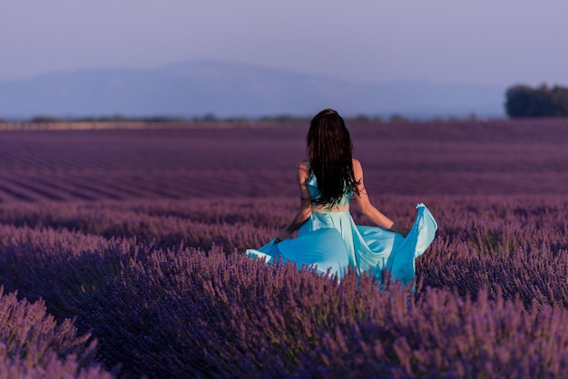 mooie jonge vrouw in cyaan jurk ontspannen en plezier maken op wind in paars lavander bloemenveld