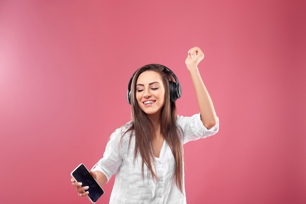 Mooie jonge vrouw in draadloze koptelefoon luisteren naar muziek met behulp van mobiel