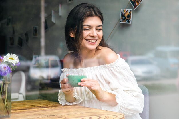 Mooie jonge vrouw in een café met een kopje koffie uitzicht vanaf de straat