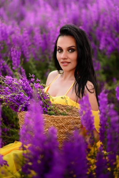 Mooie jonge vrouw in een gele jurk zit in een veld met paarse bloemen. close-up portret.