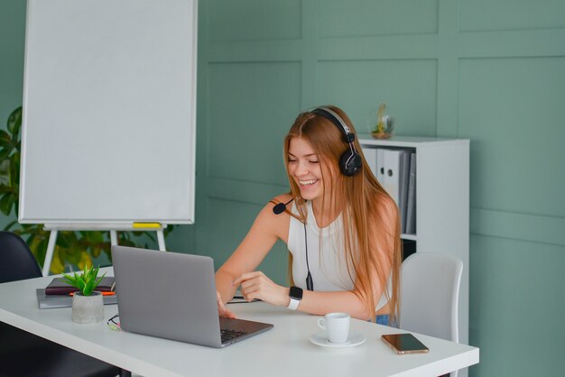 mooie jonge vrouw in een headset communiceert online met een laptop in de kantoorlevensstijl f