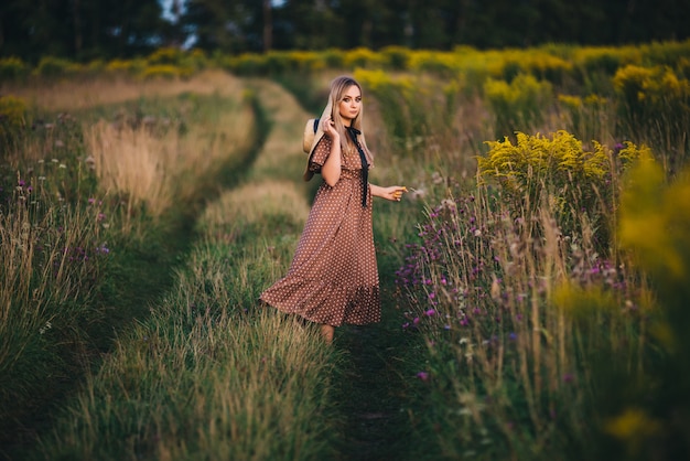 Mooie jonge vrouw in een hoed en jurk wandelingen in de natuur in de herfst.