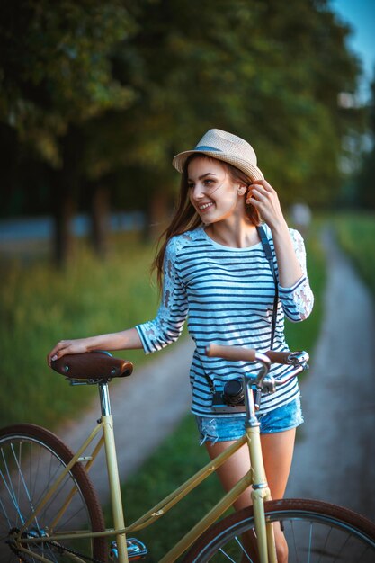 Foto mooie jonge vrouw in een hoed met een fiets in een park buiten