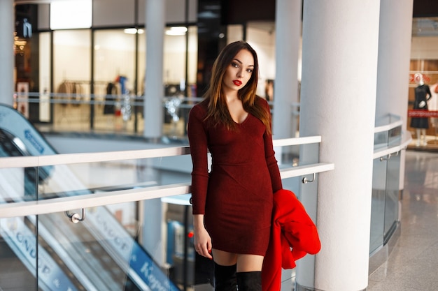 Mooie jonge vrouw in een rode jurk met een jas loopt in de winkel