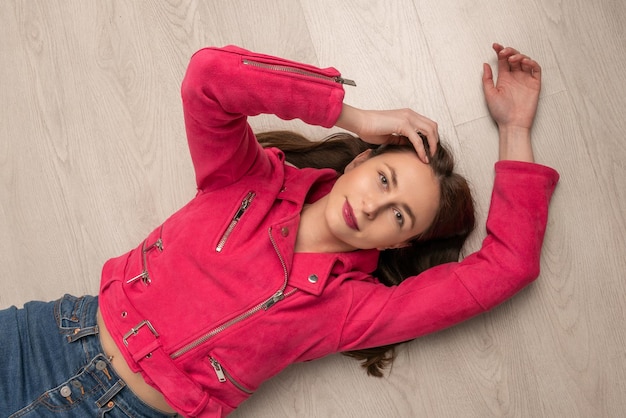 Mooie jonge vrouw in een roze jas en jeans ligt op de vloer