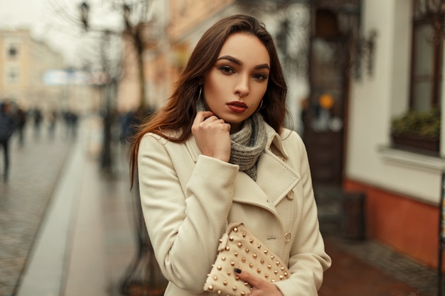 Mooie jonge vrouw in een trendy jas met een trui met een mode-tas op straat in de stad