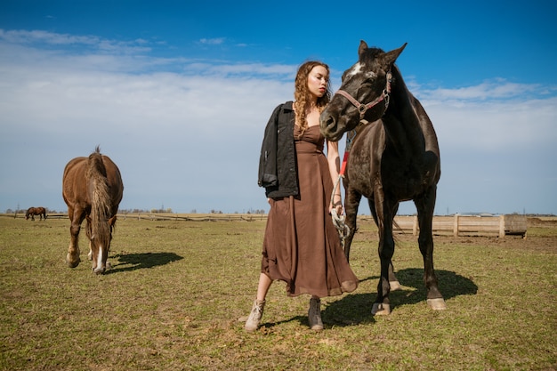 Mooie jonge vrouw in een veld met paarden. aantrekkelijk fotomodel.