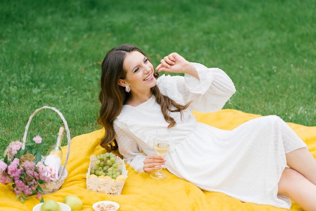 Mooie jonge vrouw in een witte jurk die wijn drinkt in de tuin op een picknick