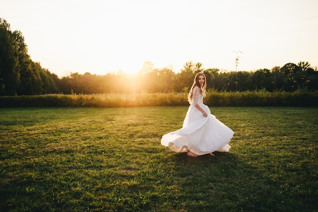 Mooie jonge vrouw in een witte trouwjurk en zwarte laarzen bij zonsondergang wordt gefotografeerd.