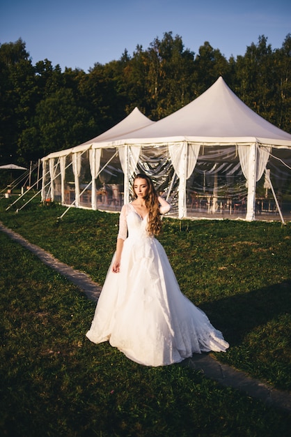 Mooie jonge vrouw in een witte trouwjurk en zwarte laarzen bij zonsondergang.