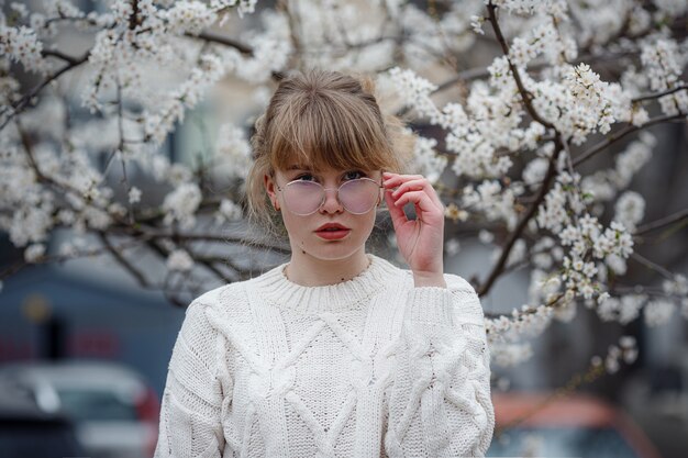 Mooie jonge vrouw in een witte trui in de kersenbloesemtuin, lentetijd. outdoor mode foto