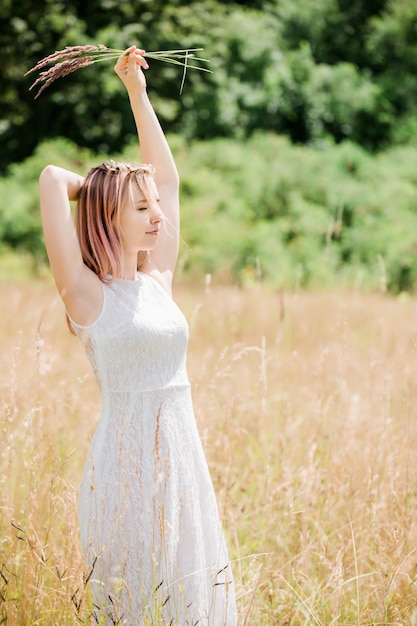 Mooie jonge vrouw in een witte vintage kanten jurk met roze haar loopt over de weide