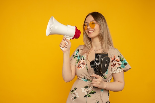 Mooie jonge vrouw in gele bril poseren met filmcamera en megafoon