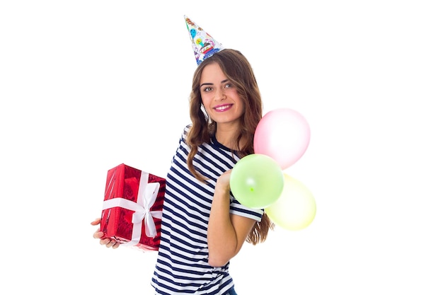 Mooie jonge vrouw in gestript T-shirt en feestmuts met rood cadeau en gekleurde ballonnen