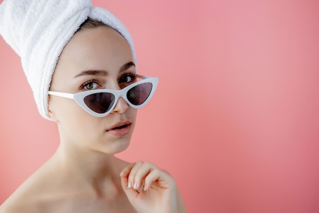 Mooie jonge vrouw in glazen met een handdoek op haar hoofd na bad op roze