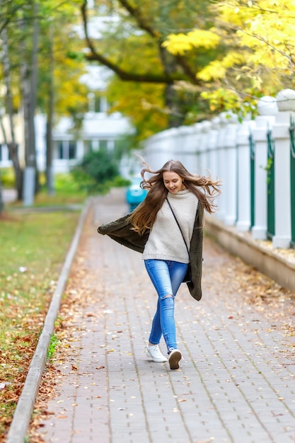 Mooie jonge vrouw in groen gebreid vest met een kap die in de herfstpark loopt