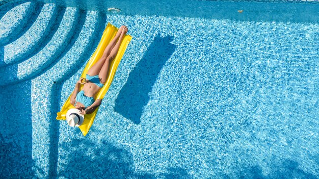 Mooie jonge vrouw in hoed in zwembad luchtfoto bovenaanzicht van bovenaf, jong meisje in bikini ontspant en zwemt op opblaasbare matras en heeft plezier in het water op familievakantie, tropische vakantieoord