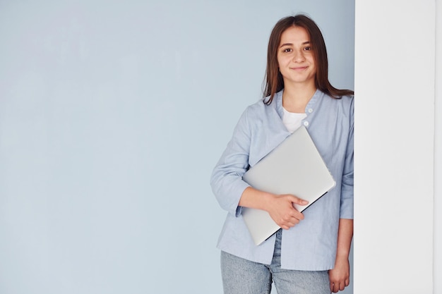 Mooie jonge vrouw in jeans en blauw overhemd die zich tegen muur met laptop in handen bevinden