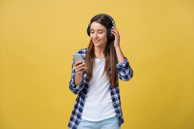 Mooie jonge vrouw in koptelefoon luisteren naar muziek en zingen op gele achtergrond.